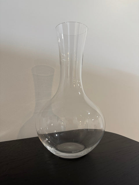 Clear crystal Riedel wine decanter with wide base and long neck on dark wooden surface