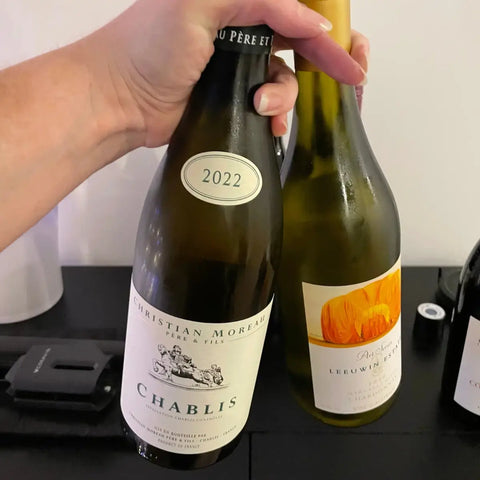 Hand holding a 2022 Christian Moreau Chablis wine bottle next to a Leeuwin Estate Art Series Chardonnay, showcasing premium French and Australian white wines.